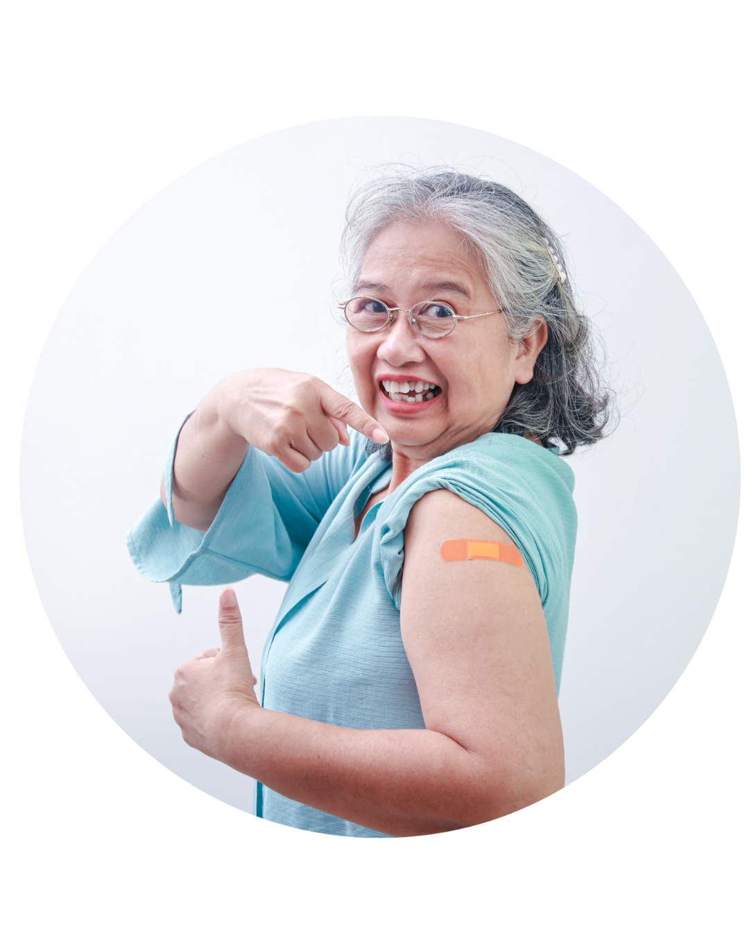 An older woman pointing to her arm with a bandage on it while smiling and giving a thumbs-up with her other hand.